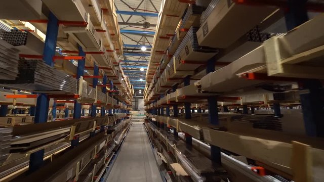 Window profiles on racks and production of windows. The camera moves along racks. Parts of window constructions in cardboard package. Then the camera drives on the shop territory on production of wind