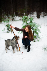 curly haired red-haired girl on a walk with a dog schnauzer in the winter afternoon in the forest