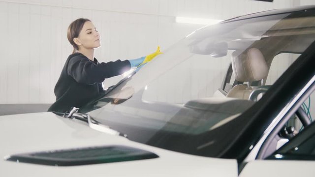 Car detailing - woman is cleaning windshield of a luxury vehicle