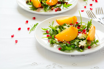 Fresh autumn salad with persimmon, arugula, cheese and pomegranate seeds on white table cloth. Space for copy