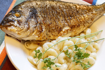 Fried fish with pasta and greens on a plate. Selective focus.