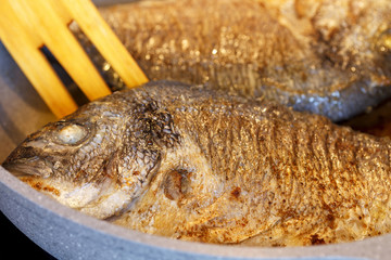 Fried Dorado fish in a frying pan. Close-up. Blurred background.