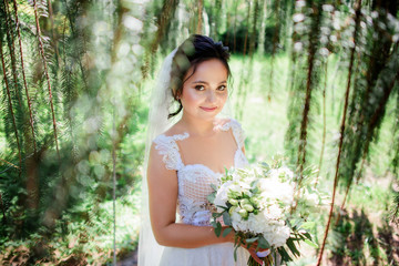 Beautiful bride in a tender dress poses with wedding bouquet in the green forest