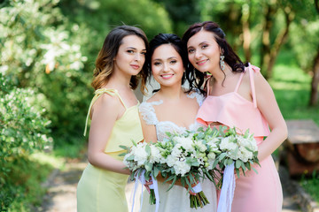 Bride and her pretty bridesmaids in pink and yellow dresses pose in the bright park