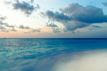 Tropical island at dawn. Beautiful bright sunrise over a tropical beach. Ocean and white sand. Clouds of gentle color over the sea.