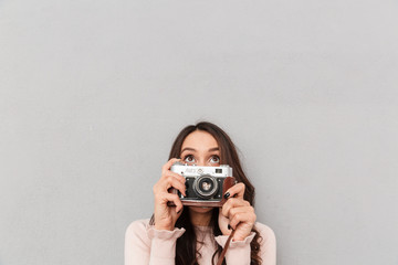 Portrait of joyful female photographer having fun while taking photos using retro camera over gray background copy space