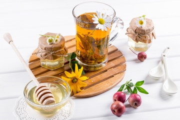 Herbal tea with herbs and flowers in a glass tea pot with honey. Bouquet of flowers on white table