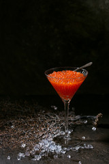 Glass of red caviar on crushed ice over dark background.
