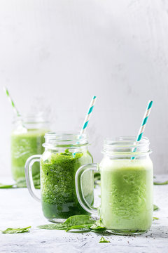 Variety of three color green spinach kale apple yogurt smoothie in mason jars with retro cocktail tubes over gray background. Healthy vegan detox eating.