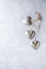 Love Valentines day greeting card with three silver hearts on rope cord over gray texture background. Top view, copy space