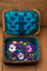 open hand-made woven straw basket (casket, box) with flowers and decorative stones inside on the wooden table