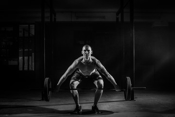 A muscular man squats with a barbell in the gym. Black and white photo