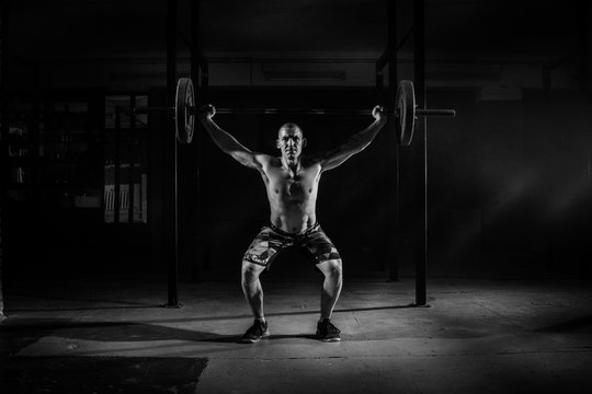 Strong man lifting a barbell in the gym. Black and white photo