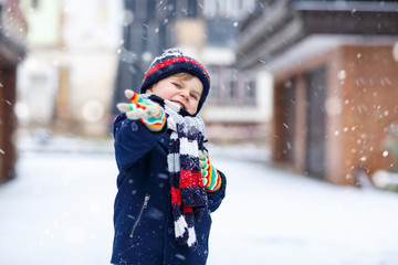 Cute little funny kid boy in colorful winter fashion clothes having fun and playing with snow, outdoors during snowfall