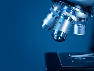 Fototapeta na wymiar Closeup lens of a modern microscope in a research lab on a dark blue background.