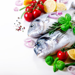 Fresh uncooked fish, dorado, sea bream with lemon, herbs, vegetables and spices on white background. Top view. Square crop