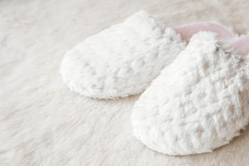 Fototapeta na wymiar Beautiful, soft, warm slippers waiting an owner on the white fluffy mat in the bedroom in the morning. Comfortable home shoes concept.