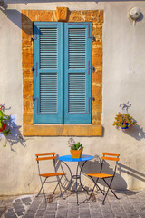 Blue shutters window and beautiful small chairs and a table on sidewalk