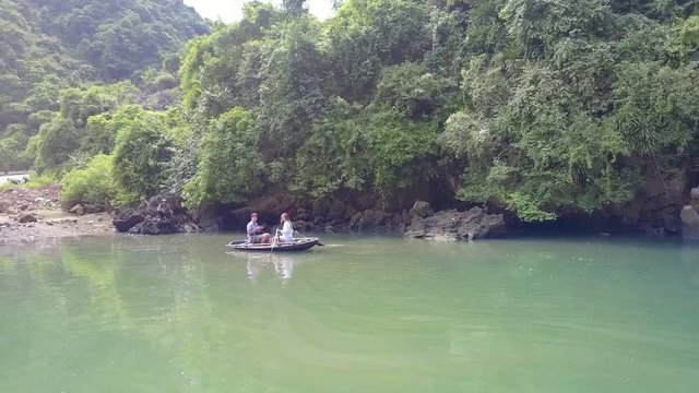 Girl Rows Boat Past Lake Bank to Dam with Road in Tourist Place