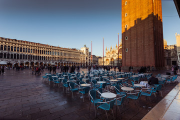 VENICE, ITALY - JANUARY 02 2018: Florian Cafe small tables in San Marco square with cathedral and bell tower shadow at evening time. Florian is an historic venetian cafe