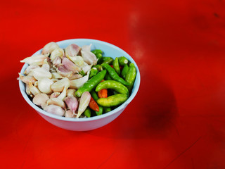 Close up perspective Thai local garlic tiny cloves with green and red small pepper chili (Chilli Padi) piled in blue melamine bowl cup, on old dirty red iron table, for eating with stewed pork leg