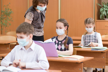 schoolchildren with protection masks against flu virus at lesson in classroom