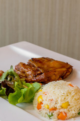 The fried rice with carrot and corn with green lettuce with piece of grilled chicken on the white panel plate on the table in restaurant , selective focus.