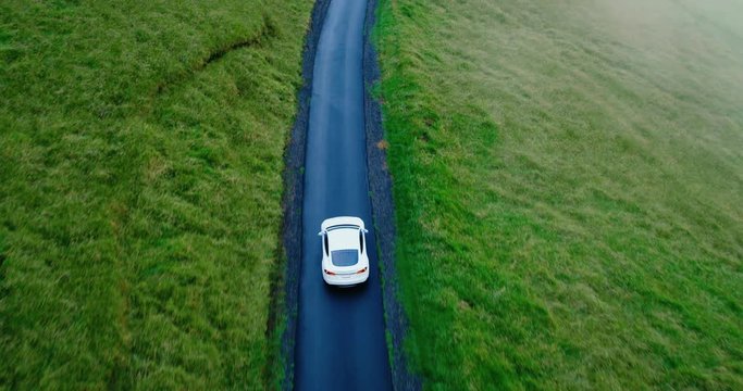 Cinematic aerial view of electric car driving on country road at sunset