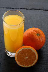 Glass of orange juice and oranges on slate board
