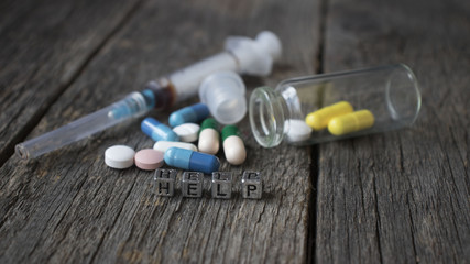 Fototapeta na wymiar bottle of pills that says help and syringe on wooden background