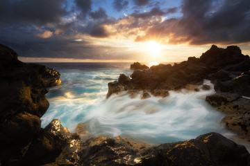 Obraz premium Coucher de soleil, vagues, roches volcaniques