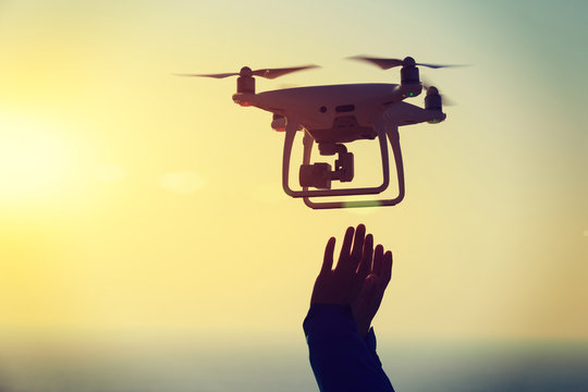 silhouette of hands reaching a flying drone which taking photo over sunrise sea