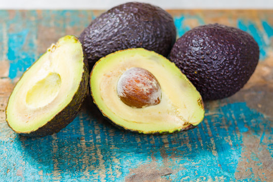 Raw ripe dark green avocados with leaves on wooden background