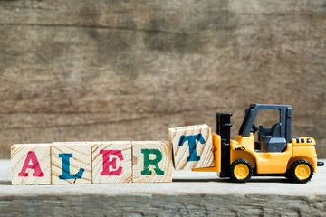 Yellow toy forklift hold letter block T to complete word alert on wood background