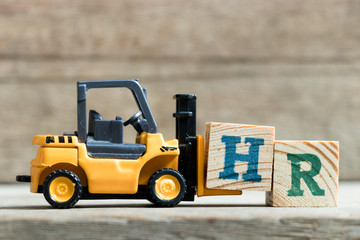 Toy yellow forklift hold letter block H to complete word HR (Abbreviation of Human resource)on wood...