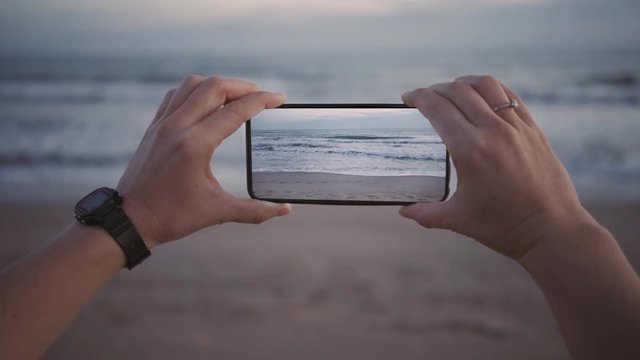 Cinemagraph of female hands hold smartphone new generation oled screen, makes photo or video for social media network, waves keep moving in loop. Inspiration to travel world