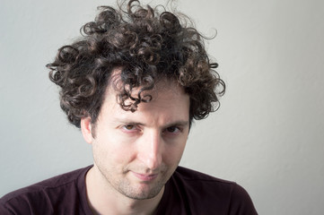 Portrait of a young, Caucasian, brunet, curly haired man looking to the camera on white background.