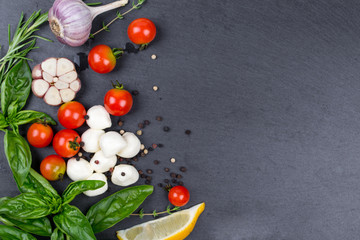 Mozzarella, cherry tomatoes and fresh basil, lemon, garlic. Ingredients for salad. On black slate stone chalkboard. Top view.