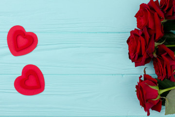 Red roses with hearts on wooden table. Bouquet of red roses and paper hearts on blue wooden background, space for text. Love and feelings concept.