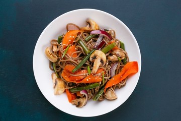 Delicious fresh pad thai noodles with mushrooms and vegetable slices on dark background, flat lay. Thai food, vegetarian meals