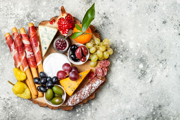 Appetizers table with antipasti snacks. Cheese and meat variety board over grey concrete background. Top view, flat lay, copy space