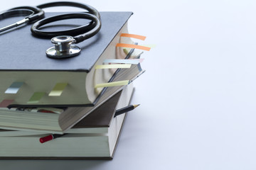Medical student textbooks with pencil and multicolor bookmarks and stethoscope isolated on white...