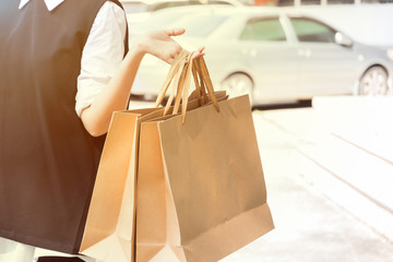 A Shopaholic Woman is holding Shopping bags by left hand with Parking lot background.