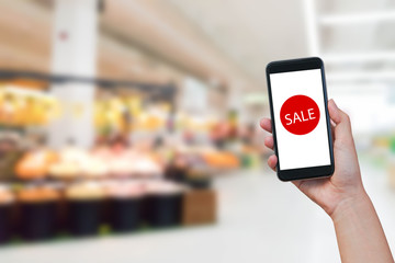 close up on woman hand holding smartphone with test 'SALE' on display over blurred supermarket for festival concept