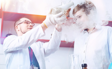 A bit of fume anyone. Curious schoolboy and a male chemistry teacher conducting an experiment in the school laboratory and having fun with a fume appearing from a vacuum flask.