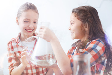 So much fun. Two young ladies getting pretty excited while holding a fuming vacuum flask and chatting about the chemical experiment held by their teacher.