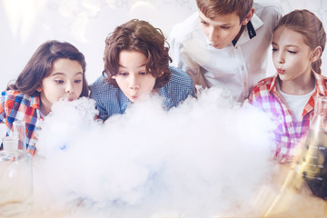 Magic is happening. Smart up and coming chemists blowing on the fume appearing after mixing several chemistry liquids together during a scientific research at school.