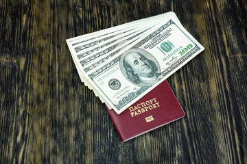 A passport with dollars lies on a wooden table.