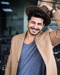 Smiling young Man with Hat and Coat looking into the camera in Munich // Lächelnder junger Mann mit Hut und Mantel in beige sieht in die Kamera in der BMW Welt in München