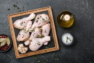 Raw chicken legs on cutting board and spices on blackboard